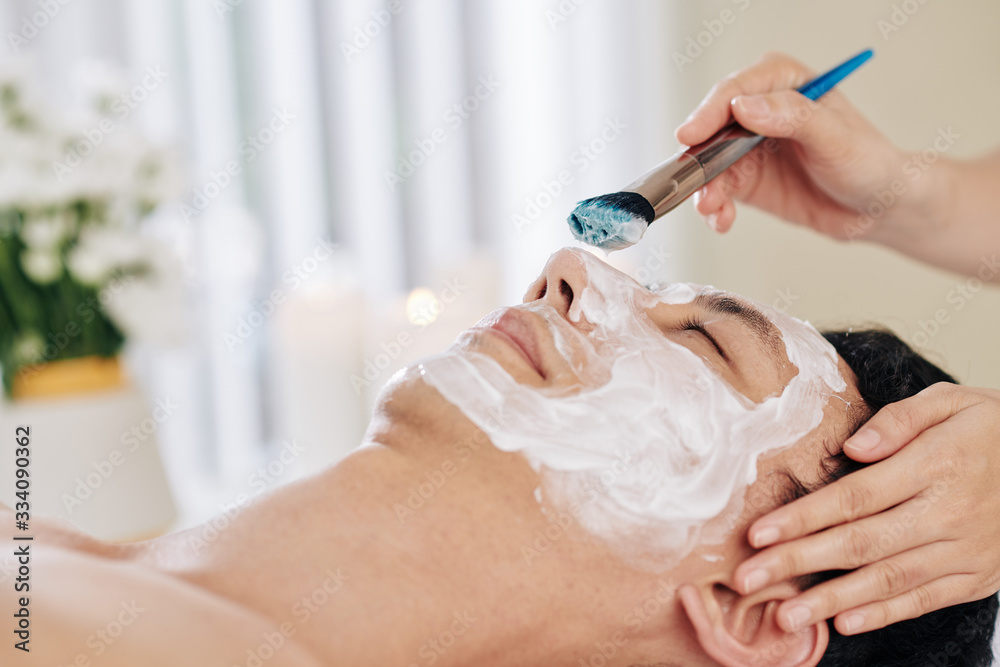 Cosmetologist applying rejuvenating mask on face of male clients Cosmetologist applying rejuvenating mask on face of male clients