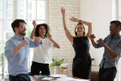 Four funny active multi-ethnic business team staff members dancing moving listening music gathered in office board room. Succeed common goal feels happy, corporate holiday event celebration concept photo
