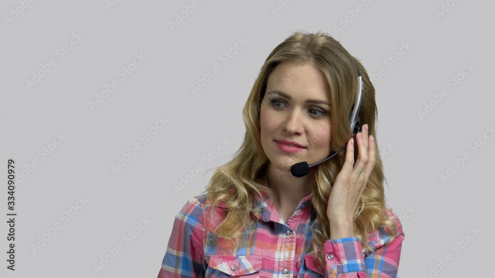 Young female operator with headset, helping client on hotline. Blond girl works in a call-center, grey isolated background. Young female operator with headset, helping client on hotline. Blond girl works in a call-center, grey isolated background.