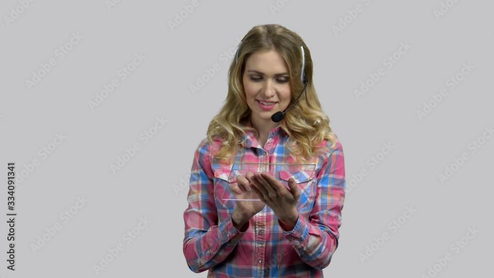 Helpdesk worker, young girl with headset and blank glass tablet. Grey isolated background. Helpdesk worker, young girl with headset and blank glass tablet. Grey isolated background.