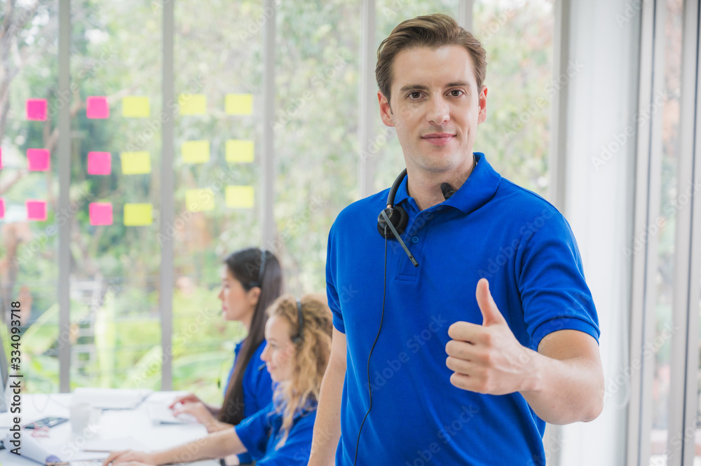 Fototapeta premium Customer support operator at work. Team Business and Delivery call center in office. Working with a headset in blue uniform while showing thumbs up.