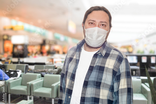 A middle-aged man in a protective mask stands in the airport lounge. The concept is the closure of borders between countries due to the risk of virus infection.