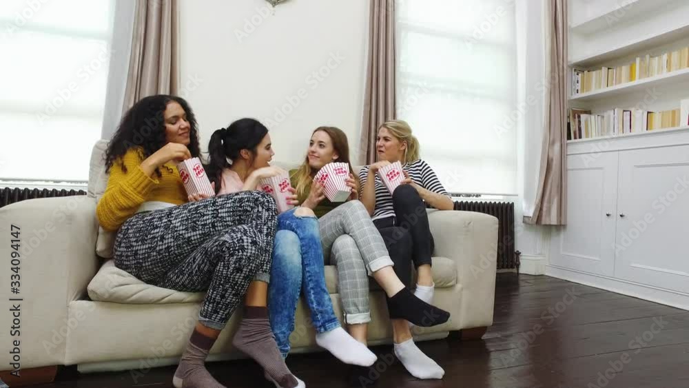 Female friends jumping on sofa and eating popcorn Female friends jumping on sofa and eating popcorn