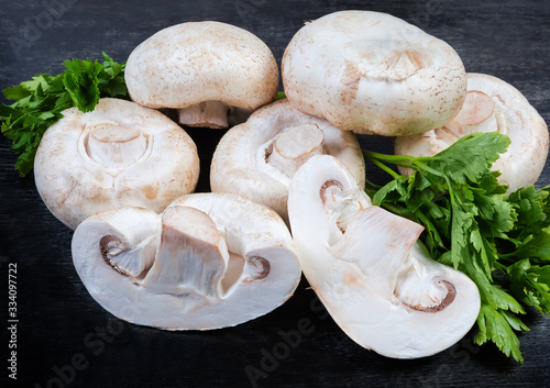 Whole and halves uncooked button mushrooms, parsley on black surface