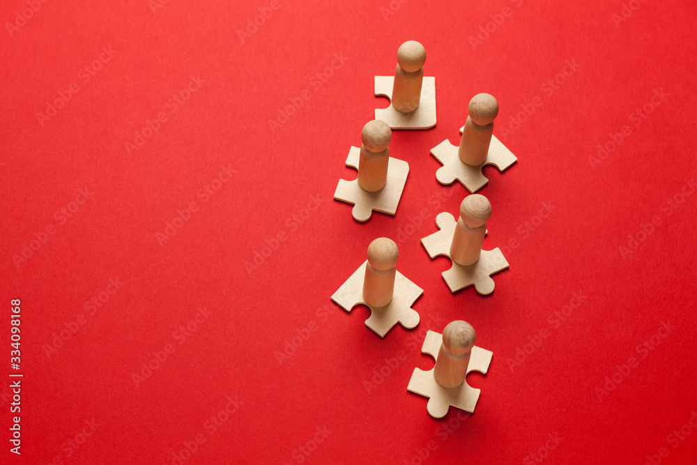 Obraz premium Wooden figures on puzzles on red background as a symbol of team building. Organization group people in business. Cooperation and partnership.