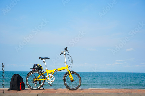 A yellow bicycle parking by the beach.  Helmet   backpack at the back and the bike.  Sports  recreation  travel  tourism including park and outdoor categories.
