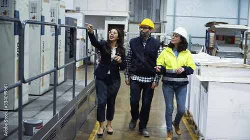 Front view of factory workers walking and talking at plant. Confident young project manager showing new five-section offset machine to technicians. Industry concept