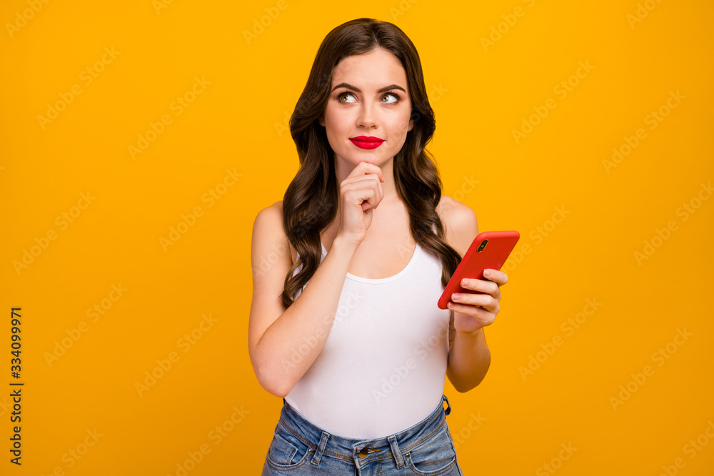 Photo of pretty lady hold telephone hands look dreamy up empty space think over new post idea arm on chin wear white tank-top jeans isolated bright yellow color background