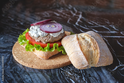 Homemade burger with beef chop, tomato, lettuce and dorblu blue cheese sauce. Serve on a wooden kitchen board on a table made of natural stone. Background image.