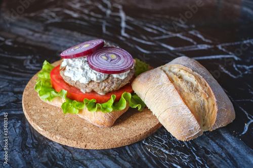 Homemade burger with beef chop, tomato, lettuce and dorblu blue cheese sauce. Serve on a wooden kitchen board on a table made of natural stone. Background image.