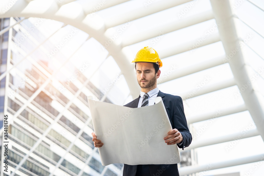 a construction manager or an architecture working and looking on his blue print seeing the construction progress, wearing suit and sit, hard hat and brainstorming idea, in a modern urban city district a construction manager or an architecture working and looking on his blue print seeing the construction progress, wearing suit and sit, hard hat and brainstorming idea, in a modern urban city district