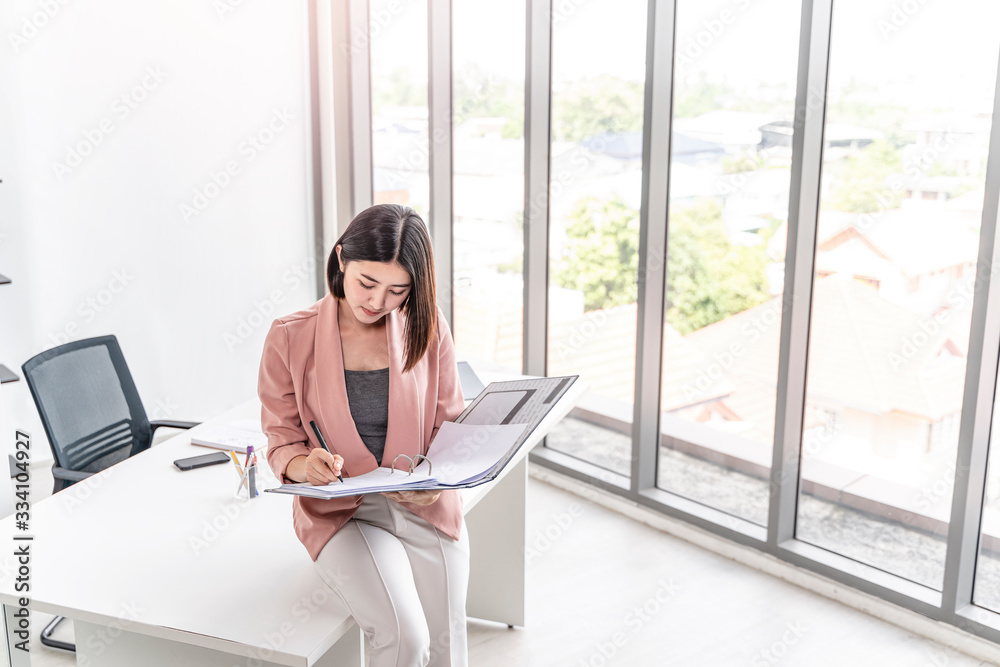 Obraz premium beautiful female asian worker holding a folder file of documents and information on work or business looking, reading, learning from the documents, while holding a pen working in an office environment