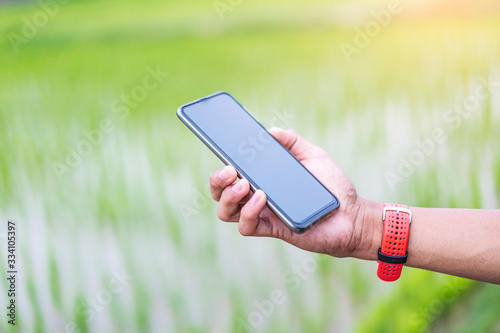 close up of asian teen runner looking at smartphone checking running distance and heart rate after exercising  wearing shirt  short and running shoes  with tree nature and cloudy sky in the background