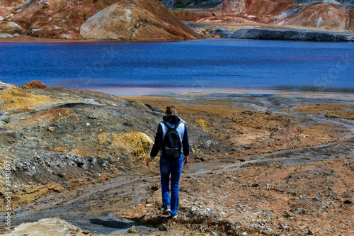 Hiking concept. Young woman goes walks among the hills, view from the back. Landscape like a planet Mars surface. Solidified red-brown black Earth surface. Copy space for text