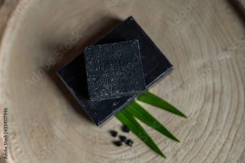 Fototapeta Naklejka Na Ścianę i Meble -  charcoal coal carbon black soap bar on a raw wood background lava stone spa skin care hygiene concept 