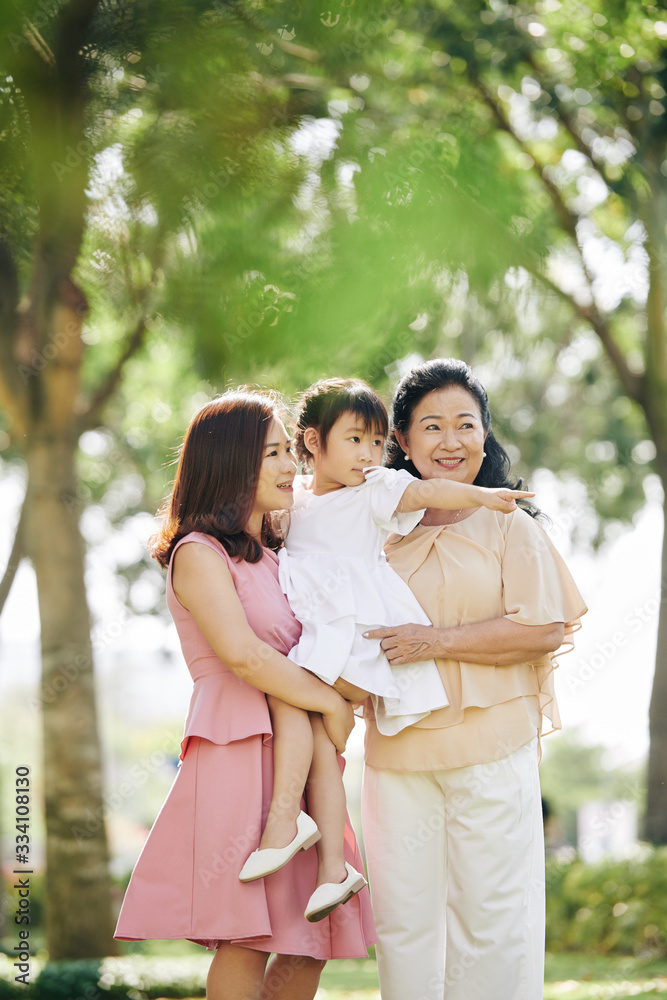 Young woman holding little daughter pointing at something interesting in city park Young woman holding little daughter pointing at something interesting in city park