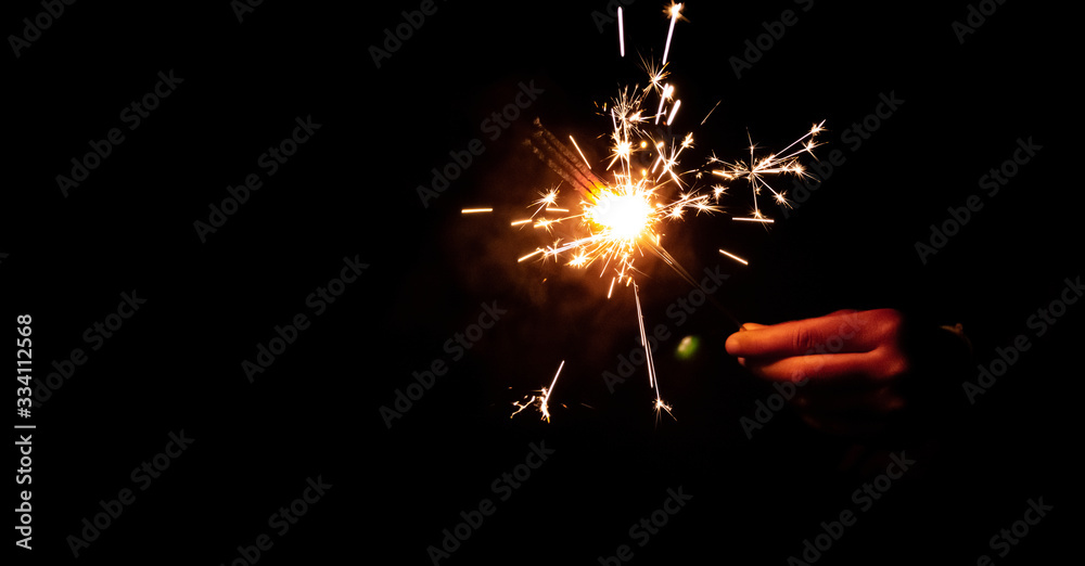 Fototapeta premium Abstract blur sparklers for celebration background,Motion by wind blurred hand holding burning Christmas sparkle on dark background.