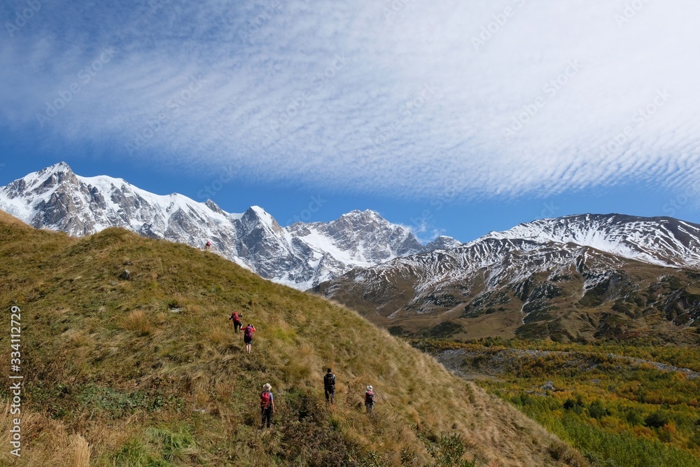 Snowy mountains Dzhangi-Tau and Shkhara with Khalde Glacier, with green mountainsides and silhouettes of wandering tourists in foreground. Greater Caucasus, Svaneti, GeorgiaSvaneti