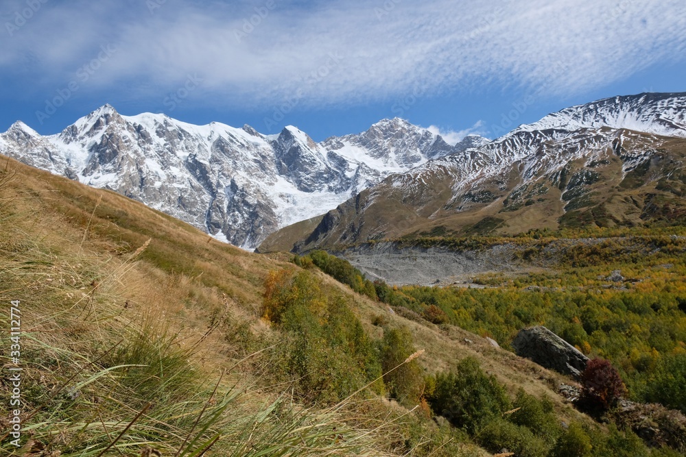 Snowy mountains Dzhangi-Tau and Shkhara with Khalde Glacier, autumn colours of mountainsides in foreground. During trekking from village of Khalde to Khalde glacier. Greater Caucasus, Svaneti, Georgia Snowy mountains Dzhangi-Tau and Shkhara with Khalde Glacier, autumn colours of mountainsides in foreground. During trekking from village of Khalde to Khalde glacier. Greater Caucasus, Svaneti, Georgia