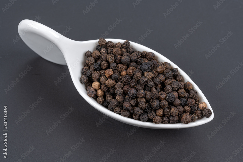 Whole black peppercorns in a white porcelain dish on a black background Whole black peppercorns in a white porcelain dish on a black background