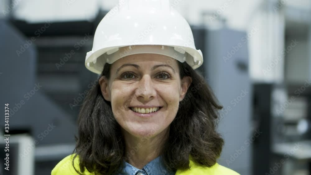 Closeup view of smiling female technician looking at camera. Cheerful mature engineer posing at factory. Manufacturing employee concept Closeup view of smiling female technician looking at camera. Cheerful mature engineer posing at factory. Manufacturing employee concept