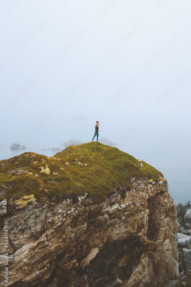 Woman standing alone on rocky cliff  travel vacation adventure lifestyle outdoor isolation solitude depression concept foggy landscape seaside in Norway