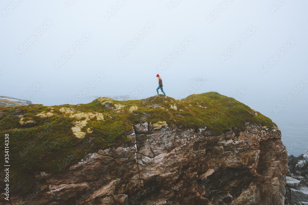 Woman walking alone on cliff rock travel lifestyle adventure vacations outdoor isolation solitude concept foggy landscape in Norway