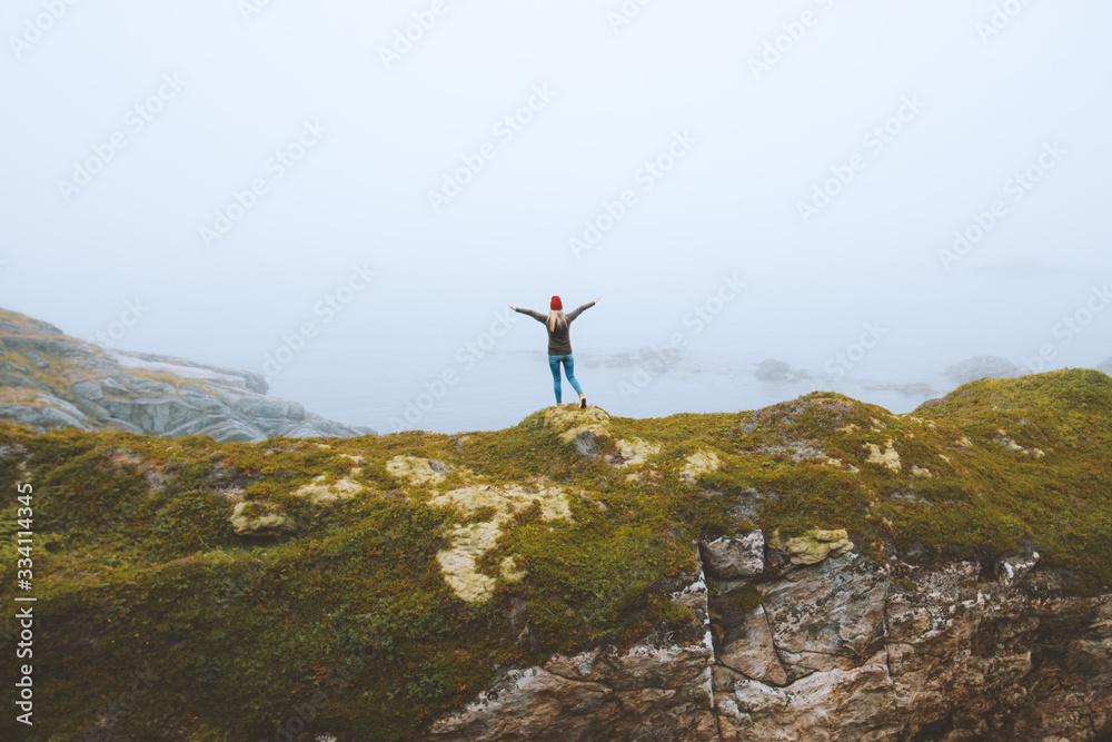 Woman traveler alone on seaside cliff travel lifestyle adventure vacations outdoor girl raised hands foggy landscape in Norway Woman traveler alone on seaside cliff travel lifestyle adventure vacations outdoor girl raised hands foggy landscape in Norway
