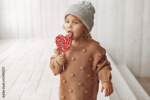 Child in a studio. Little girl with a candy. Girl in a brown sweater. photo