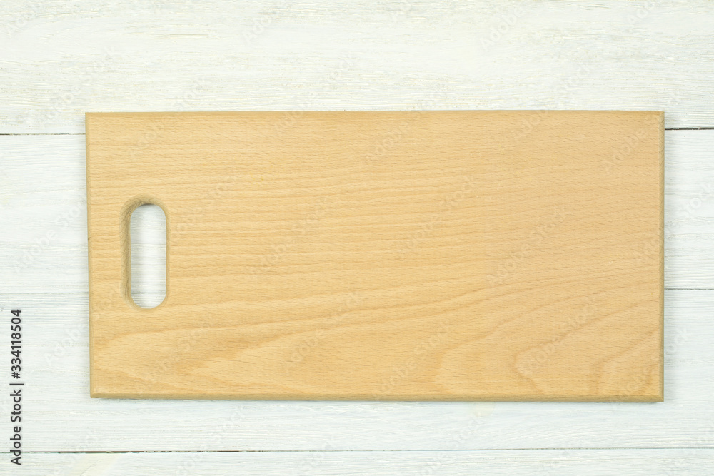 Light color cutting board lies on a white wooden background.