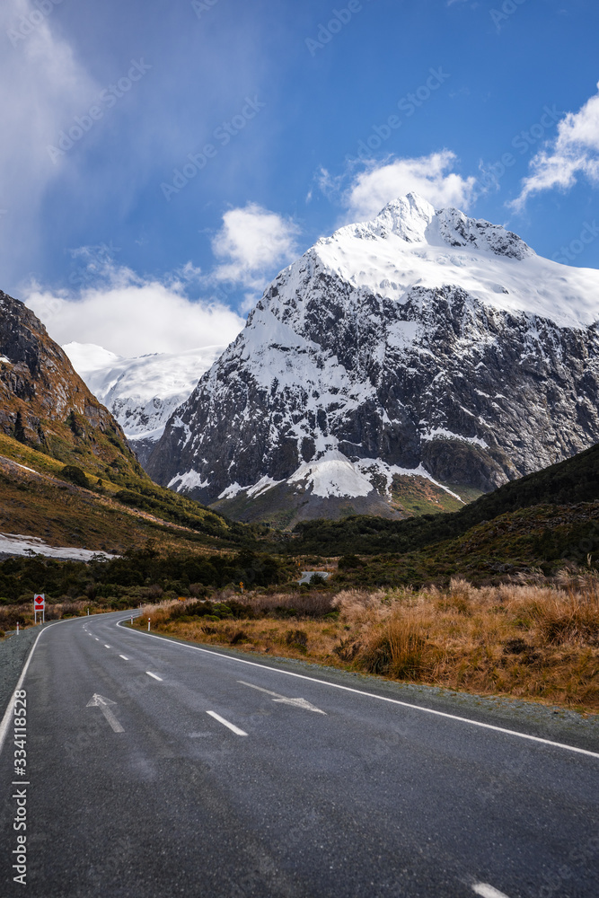 Fototapeta premium Splendid image of the SH94 road towards Milford Sound surrounded by greenery with snow capped mountains in the background taken on a sunny winter day, New Zealand