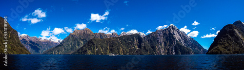 Beautiful panorama of Milford Sound with Mitre Peak on the foreground and snow capped mountains in the background taken on a sunny spring day, New Zealand © RG41_official