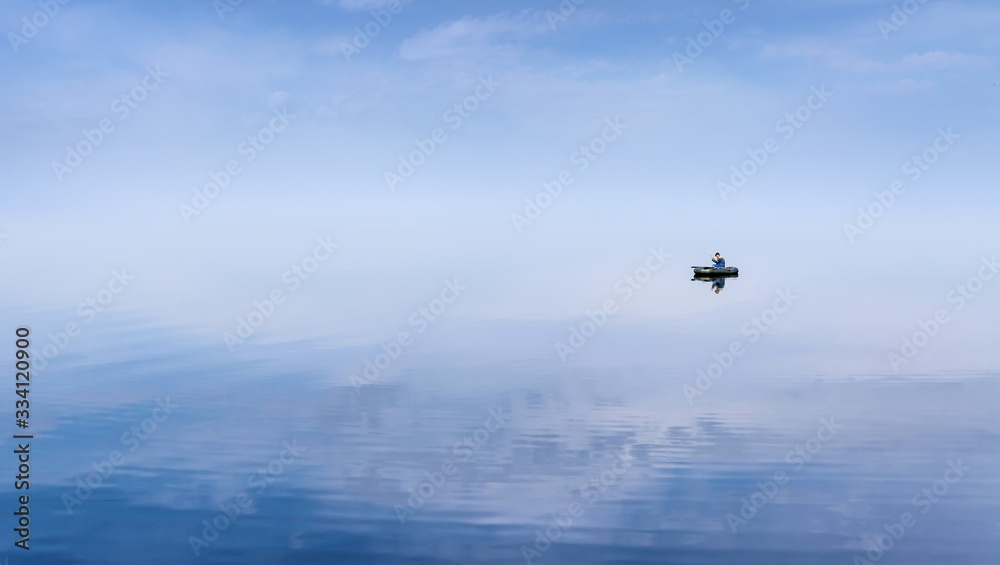 Mirror Surface Lake with a Lone fisherman on an inflatable boat and mice blue sky on background