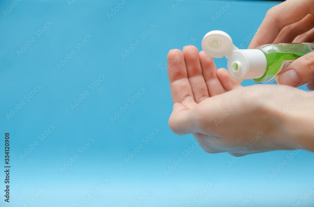 Women's hands using green antibacterial hand gel close up on blue background with copy space
