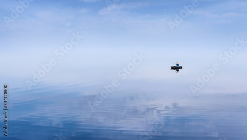 Mirror Surface Lake with a Lone fisherman on an inflatable boat and mice blue sky on background © maximchuk