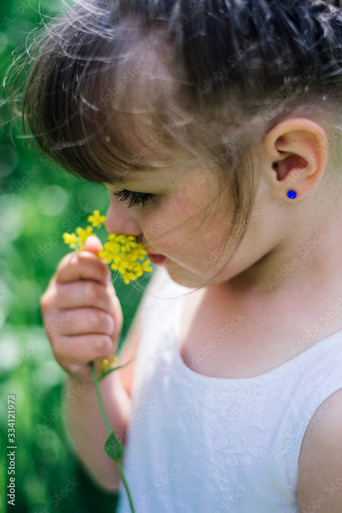 A little girl in dress sniffing flowers in the garden.Portrait of smiling cute little girl outdoors.little girl sniffs flowers with her eyes closed. A little girl in dress sniffing flowers in the garden.Portrait of smiling cute little girl outdoors.little girl sniffs flowers with her eyes closed.