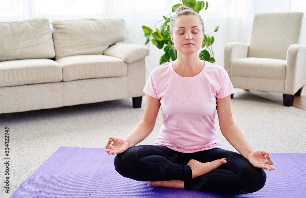 Girl sitting in lotus position and meditating at home interior, copy space. Padmasana. Woman practicing home yoga. Close up hands in meditating gesture. Freedom concept