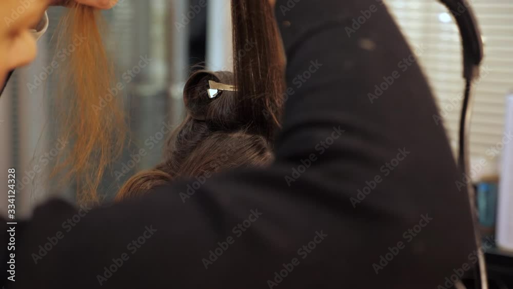 Close up professional hairstylist makes waves curling on a woman's hair. The girl in the beauty salon takes a lock of hair and presses it with a hair straightener. 4K footage Close up professional hairstylist makes waves curling on a woman's hair. The girl in the beauty salon takes a lock of hair and presses it with a hair straightener. 4K footage