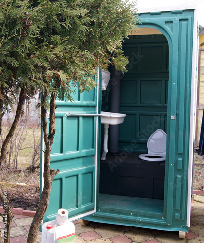 Cabin of a plastic biotoilet with an open door behind a juniper bush in the country photo