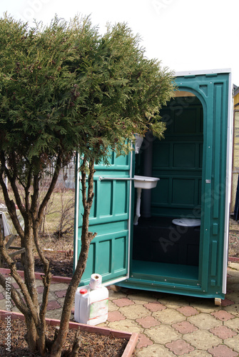 Cabin of a plastic biotoilet with an open door behind a juniper bush in the country photo