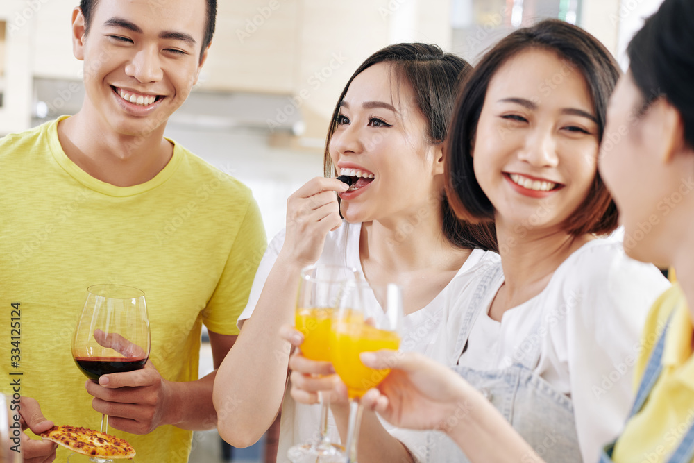 Pretty smiling young Asian woman eating olive and having drink at house party with friends Pretty smiling young Asian woman eating olive and having drink at house party with friends