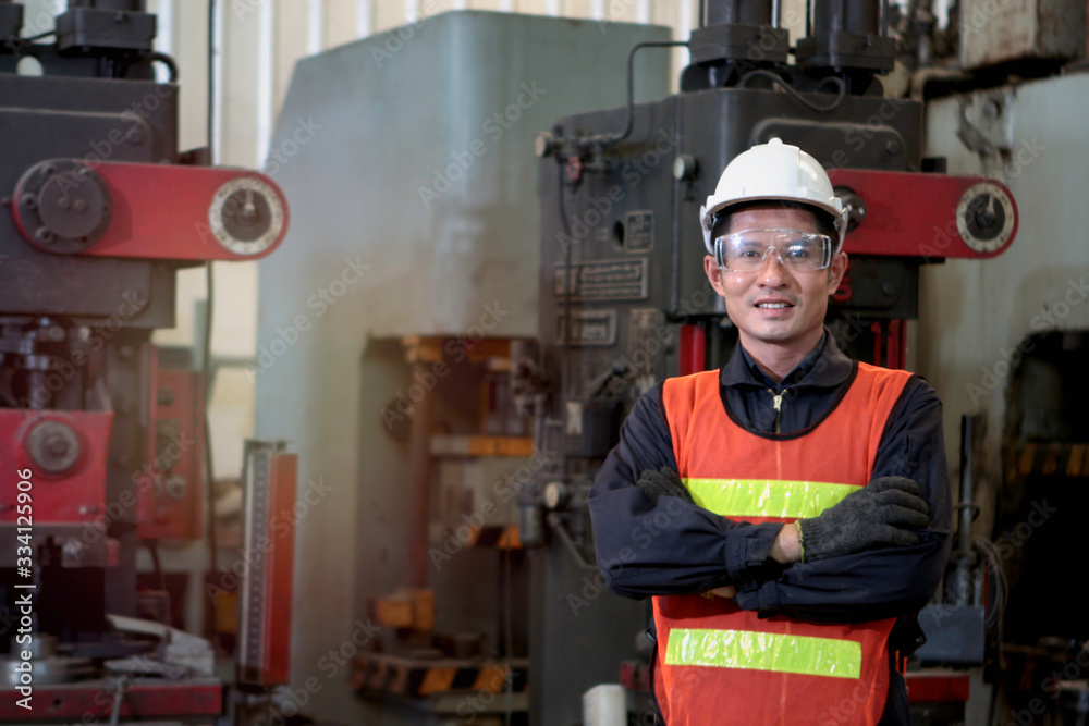 Industrial engineer worker wearing helmet and safe glasses standing with arms crossed at manufacturing plant factory, working with machine in industry concept
