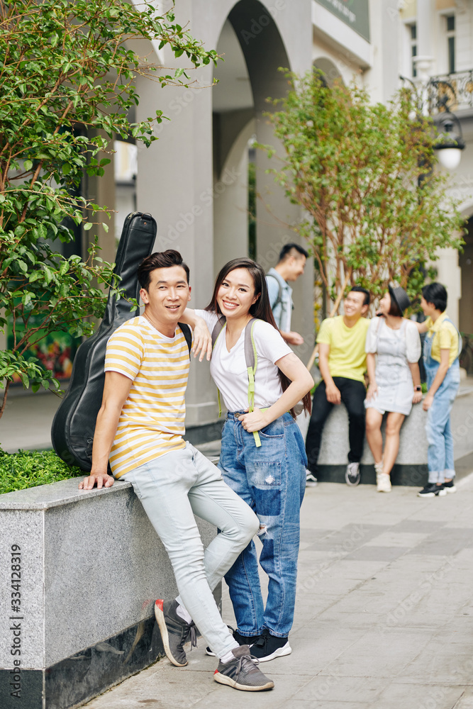 Fototapeta premium Cheerful Vietnamese college students standing at campus entrance and looking at camera