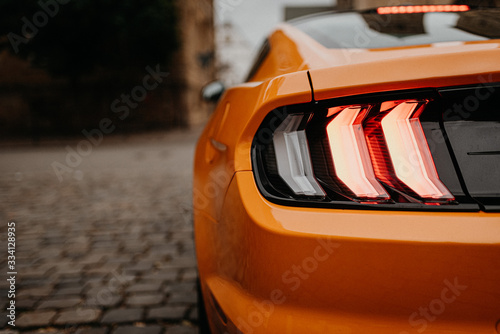 Fotografia rear lights of orange car on the street from behind with copy space