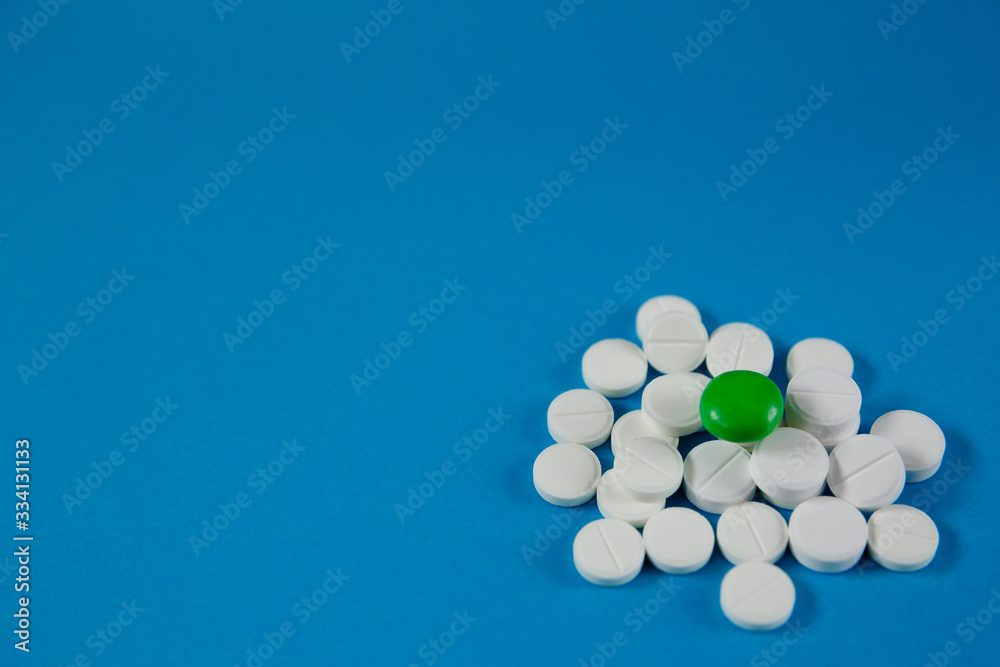 heap of white pills and one green, on a blue background