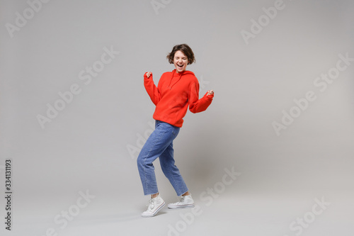 Side view of joyful young woman girl in casual red hoodie blue jeans posing isolated on grey background. People lifestyle concept. Mock up copy space. Clenching fists like winner keeping eyes closed.