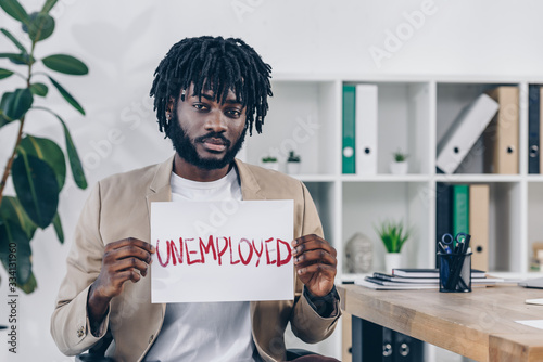 African american employee looking at camera and presenting placard with unemployed lettering in office © LIGHTFIELD STUDIOS