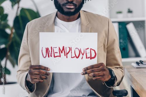 Cropped view of african american employee showing placard with unemployed lettering in office photo