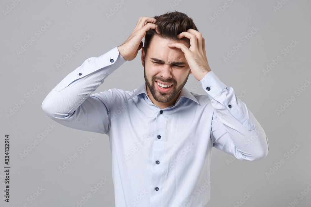Sick exhausted young unshaven business man in light shirt posing isolated on grey wall background. Achievement career wealth business concept. Mock up copy space. Put hands on head, having headache. Sick exhausted young unshaven business man in light shirt posing isolated on grey wall background. Achievement career wealth business concept. Mock up copy space. Put hands on head, having headache.