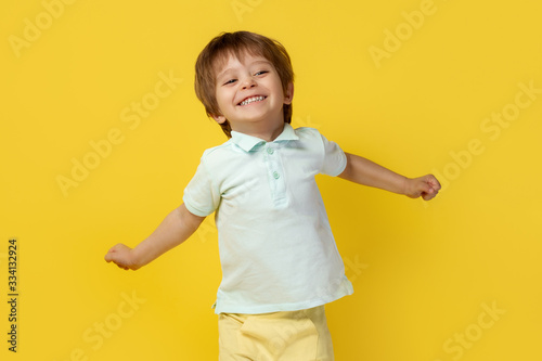 Adorable little kid in casual summer outfit with bright smile stretching out arms over yellow background.